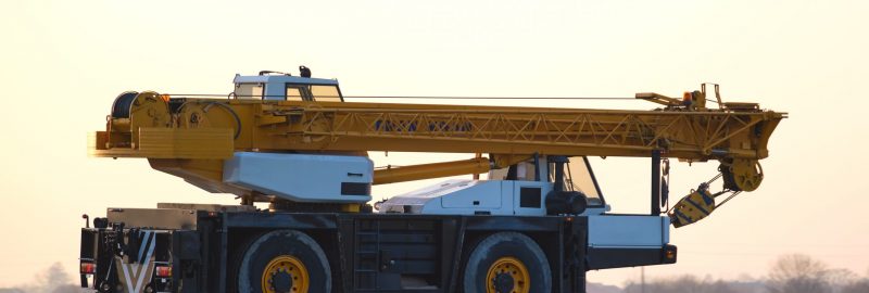 Heavy duty mobile lifting crane driving on intercity road at sunset.